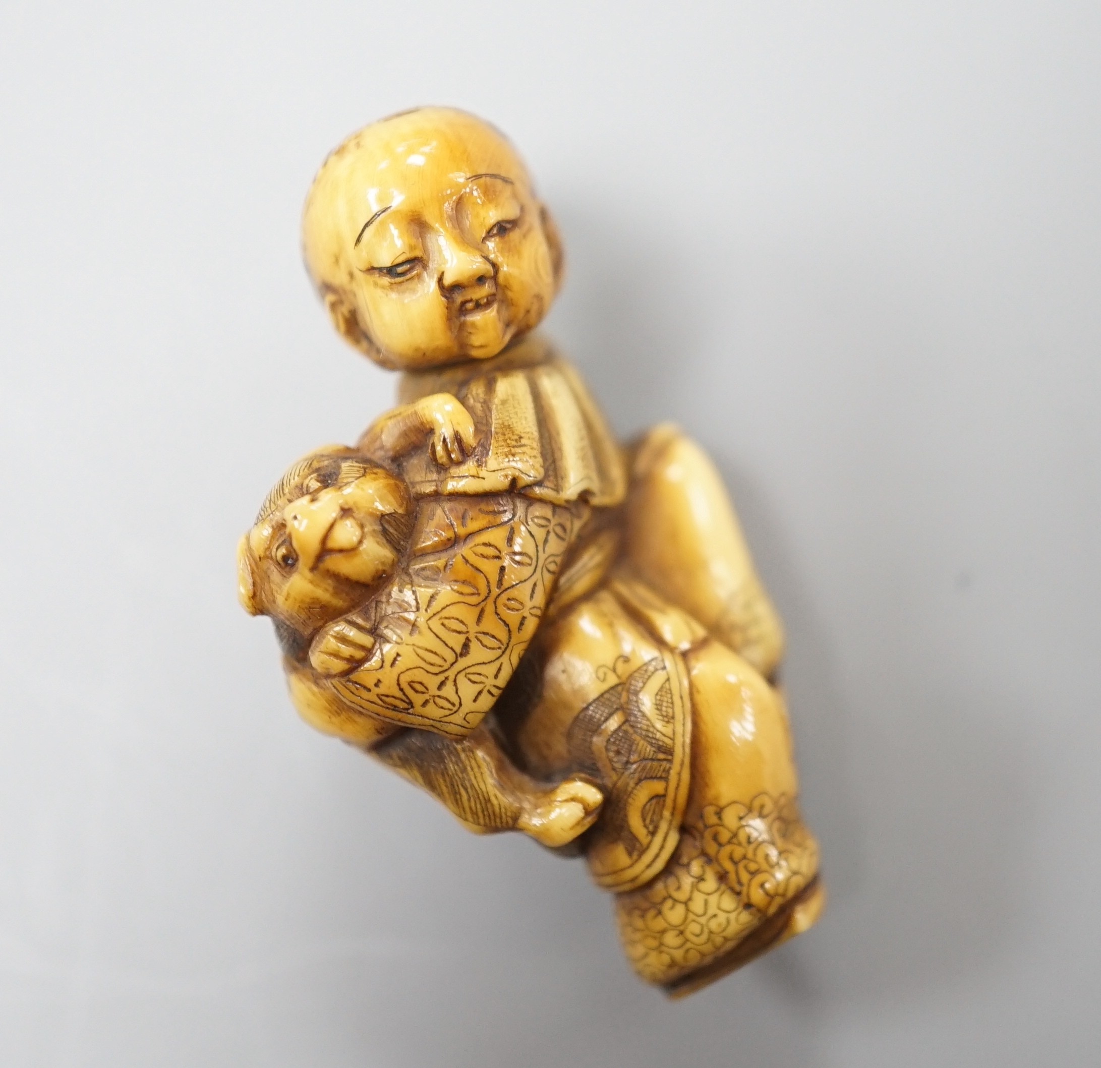 A Japanese ivory netsuke of a dog piggybacking a boy, Meiji period, 3.9cm